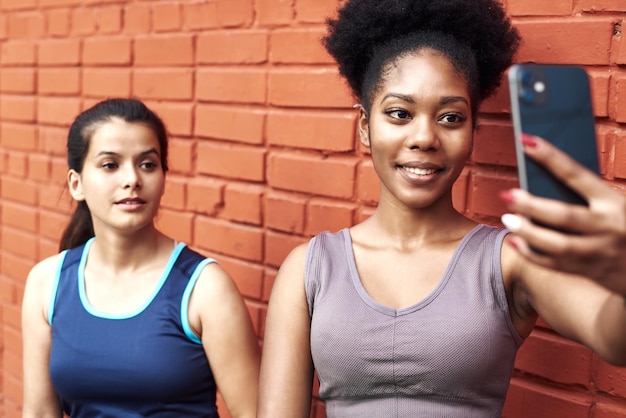 Afbeelding van geweldige jonge atletische vrouwen die een selfie maken tegen een bakstenen muur Glimlachende zwarte vrouwen brengen samen tijd door na het sporten