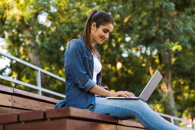 Afbeelding van geweldige jonge mooie vrouw buiten zitten met behulp van laptopcomputer.