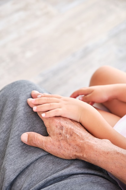 Afbeelding van handen van grootvader en kleindochter geklemd op de benen met een gladde vloerachtergrond met natuurlijk licht