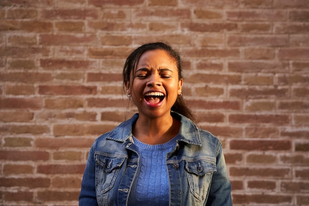 Afbeelding van jonge African American vrouw schreeuwen opgewonden met gesloten ogen staande geïsoleerd over een bakstenen muur.