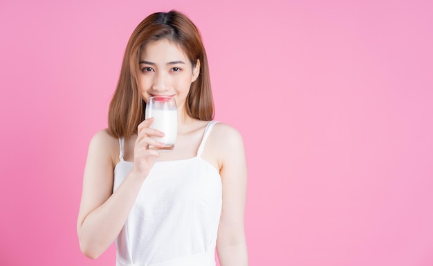 Afbeelding van jonge Aziatische vrouw die melk drinkt op roze achtergrond