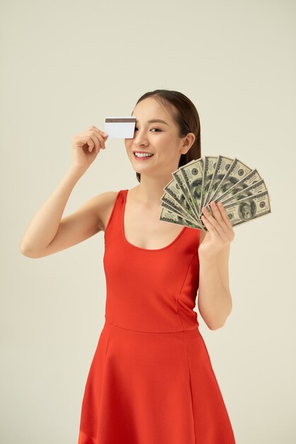 Afbeelding van jonge Aziatische vrouw met geld bankbiljetten en creditcard geïsoleerd over grijze achtergrond
