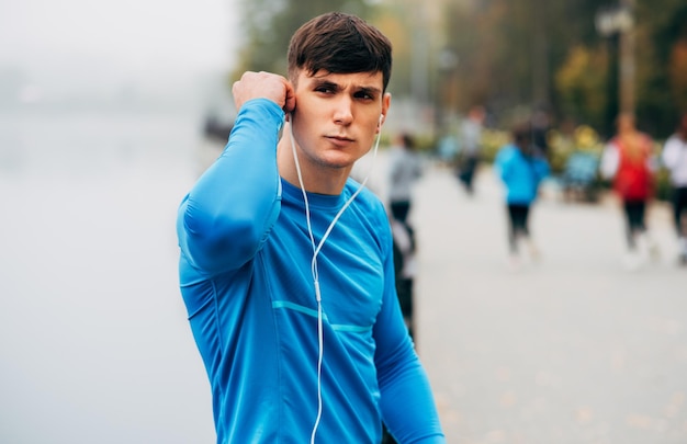 Foto afbeelding van jonge jogger gespierde man die zich uitstrekt buiten in de ochtend op de mist natuur achtergrond fitness man oefenen in het park en luisteren naar de muziek op oortelefoons mensen en sport concept