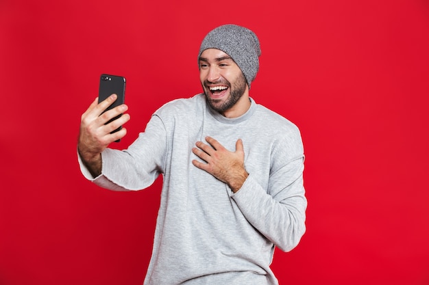 Afbeelding van jonge man 30s met baard en snor smartphone terwijl staande houden, geïsoleerd