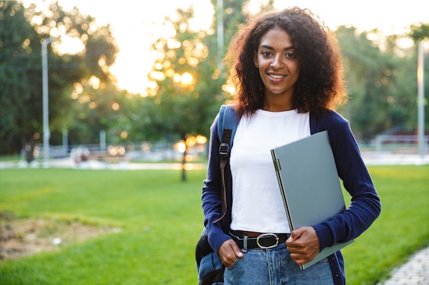 Afbeelding van jonge mooie Afrikaanse vrouw student wandelen in het park met laptopcomputer.