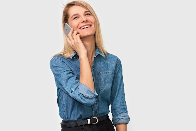Afbeelding van jonge mooie blonde vrouw in denim overhemd glimlachend en pratend op slimme telefoon met haar vriend op zoek vrolijk en gelukkig poseren op witte studio achtergrond Echte menselijke emoties