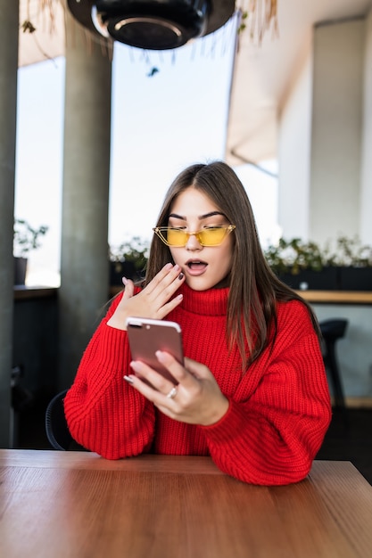 Afbeelding van jonge vrouw die sms leest aan de telefoon in café