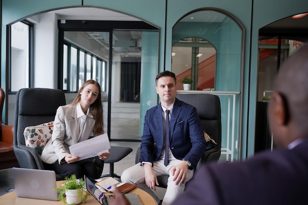 Afbeelding van jonge zakenlieden en collega die document in laptop en touchpad bespreken tijdens vergadering