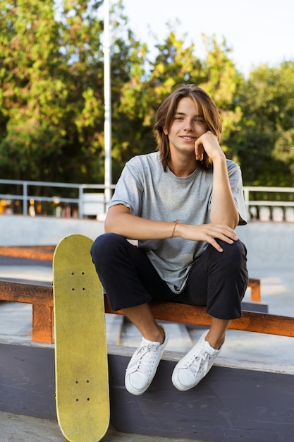 Afbeelding van knappe jonge skater man zitten in het park met skateboard.
