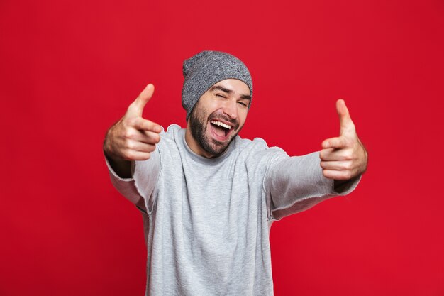 Afbeelding van lachende man 30s met baard en snor wijzende vingers naar je terwijl je staat, geïsoleerd