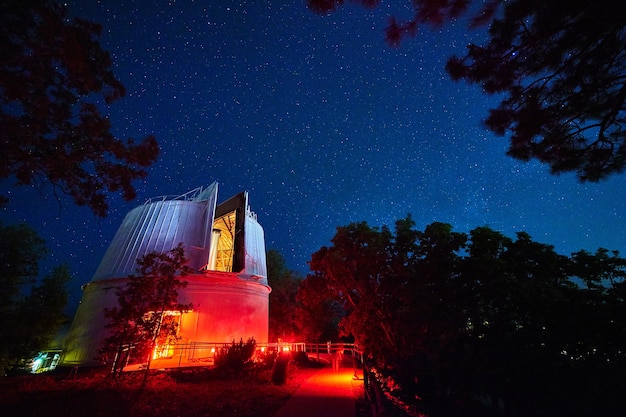 Afbeelding van landschap van een observatorium verlicht in rood en blauw licht 's nachts met bomen op de achtergrond