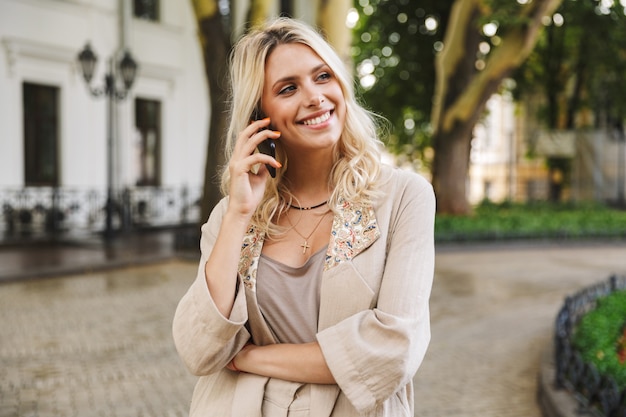 Afbeelding van mooie vrouw dragen pak met behulp van mobiele telefoon voor oproep, tijdens het wandelen door stadsstraat