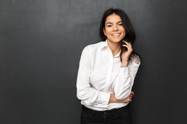 Afbeelding van mooie vrouw, gekleed in zakelijke outfit glimlachen, geïsoleerd over donkergrijze muur