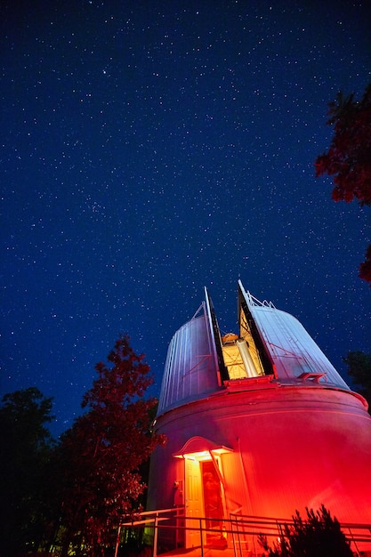 Afbeelding van Observatory verlicht in rode en blauwe lichten 's nachts omringd door bomen