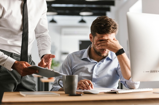 Foto afbeelding van ontevreden zakenman problemen op het werk zittend door de tafel in kantoor