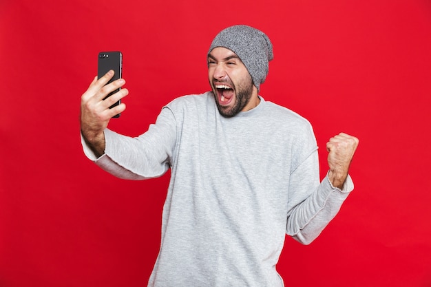 Afbeelding van opgewonden man 30s met baard en snor die smartphone terwijl hij staat, geïsoleerd