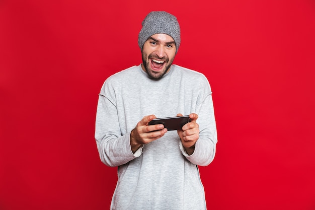 Afbeelding van optimistische man 30s smartphone houden en spelen van videogames, geïsoleerd