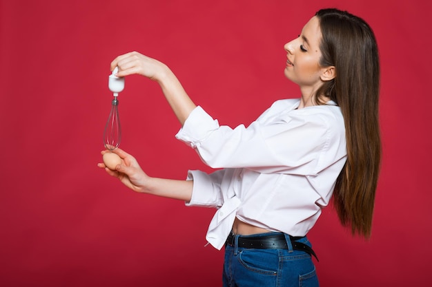 Afbeelding van schreeuwende opgewonden positieve jonge vrouw chef-kok met garde en eieren geïsoleerd op roze