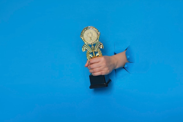 Afbeelding van trofee in hand concept voor winnen of succes Gouden trofee op blauwe achtergrond bovenaanzicht met ruimte voor tekst