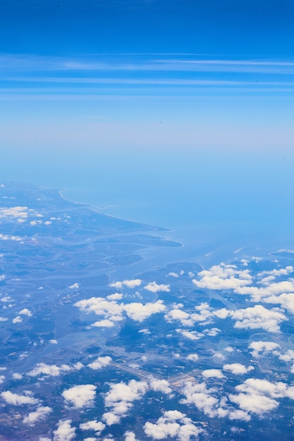 Afbeelding van vliegtuigzicht op wolken en blauwe lucht met land in de verte