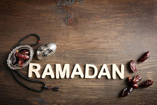 Afbeelding van woord RAMADAN met rozenkrans en dadels fruit op houten achtergrond close-up