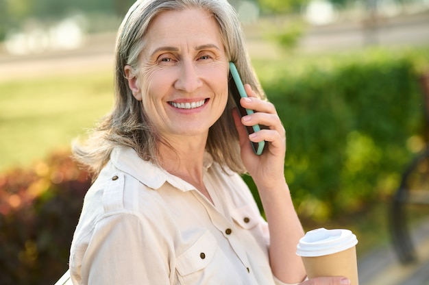 Affabile donna sorridente che comunica tramite smartphone