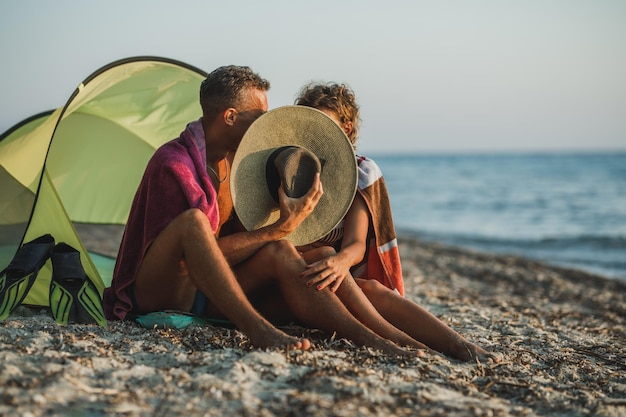 An affectionate couple enjoying day at the beach and kissing behind a straw hat.