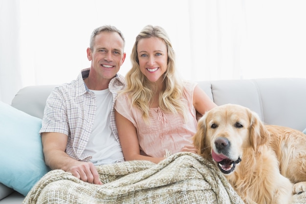 Ласковая пара, сидя на диване под одеялом с их собакой