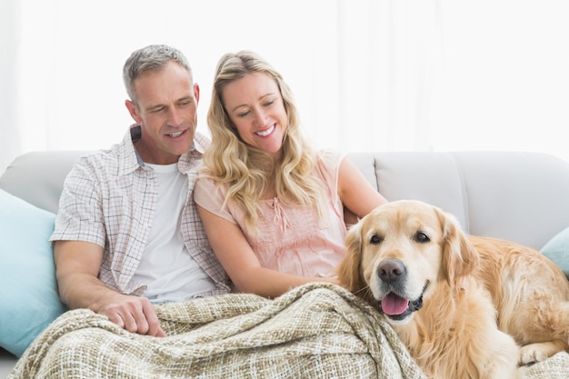 Ласковая пара, сидя на диване под одеялом с их собакой