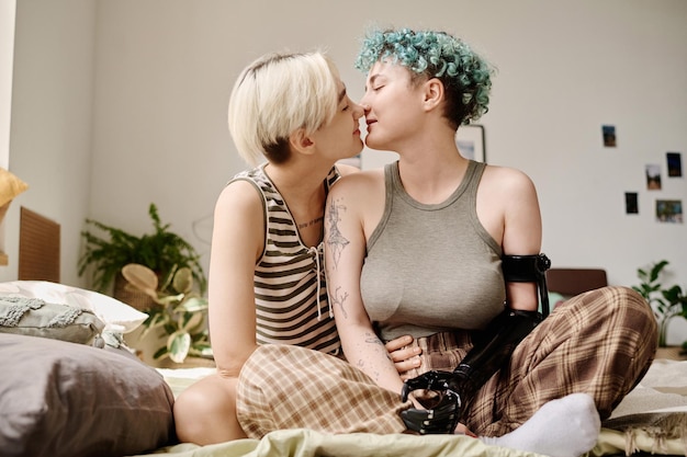 Photo affectionate lesbian couple sitting on bed in bedroom and kissing