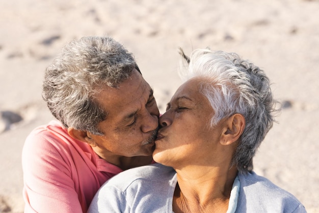 ビーチで晴れた日を楽しみながら、唇にキスをする愛情深い多民族の老夫婦