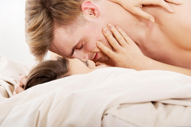 Affectionate shirtless couple kissing while lying on bed at home