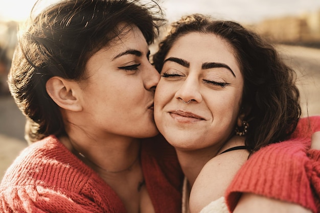 Affectionate Teen women best friends kissing on the cheek and hugging outdoors