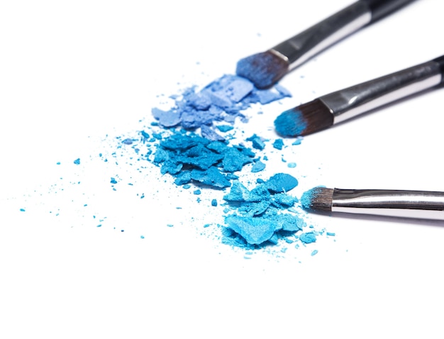 Afgebrokkelde compacte blauwe oogschaduw verschillende tinten met make-upborstels op witte achtergrond