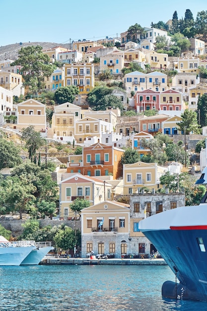 Afgemeerd jacht op zee tegen de oude stad met veelkleurige gebouwen verspreid over heuvels op het eiland Symi