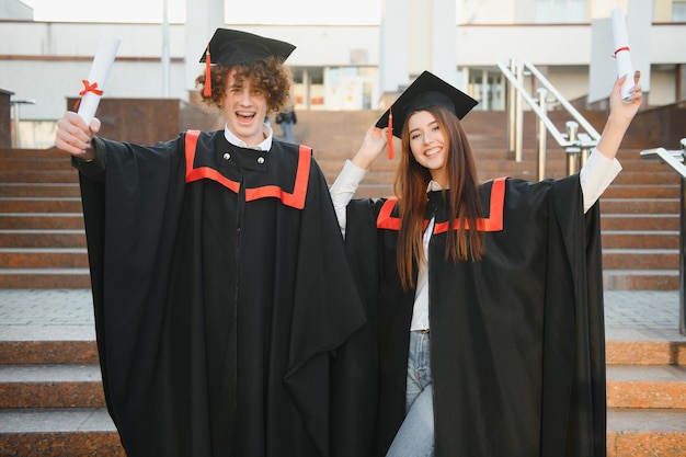 Afgestudeerden in mantels met diploma's in handen staan in de buurt van de universiteit