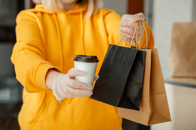 Afhaalmaaltijden papieren zak, kopje koffie of drankje. Lunchpakket met lunchpakket om mee te nemen in afhaalrestaurant. Keukenmedewerker geeft online bestellingen in handschoenen. Contactloos eten bezorgen.