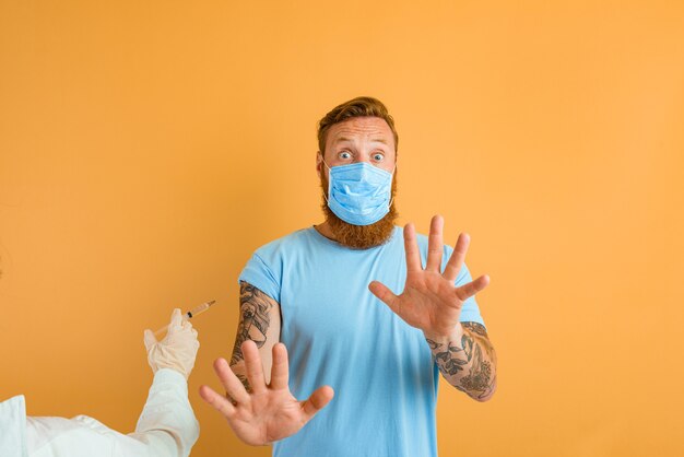 L'uomo impaurito con barba tatuaggio e maschera per covid è pronto per il vaccino contro il virus