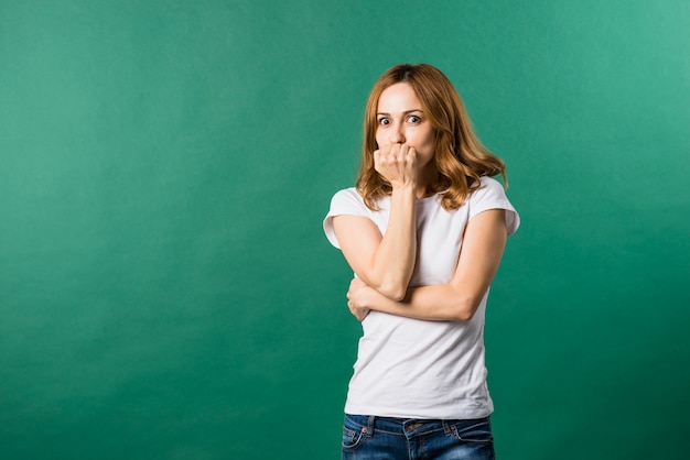 Afraid young woman covering her mouth against green backdrop