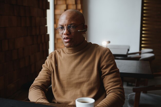 Photo african-ameican entrepreneur wearing shirt with rolled up sleeves looking through window with thoughtful and serious face expression, feeling nervous before meeting with business partners at cafe