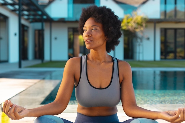 African american afro young woman looking away while practicing yoga on poolside. Unaltered, healthy lifestyle, yoga, fitness and active lifestyle concept.