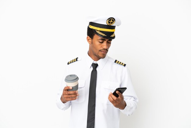 African American Airplane pilot over isolated white background holding coffee to take away and a mobile