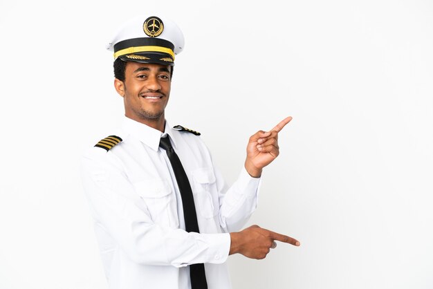 横に指を指して製品を提示する孤立した白い背景の上のアフリカ系アメリカ人の飛行機のパイロット