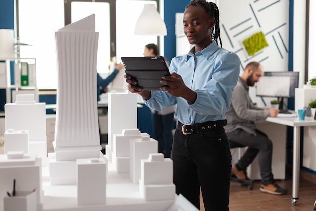 african american architect woman working on tablet looking at building maquette