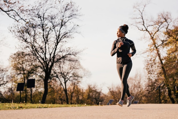 African American athletic woman running in autumn day at the park Copy space