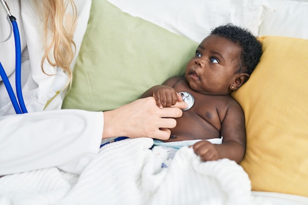 African american baby having medical examination sitting on bed at bedroom