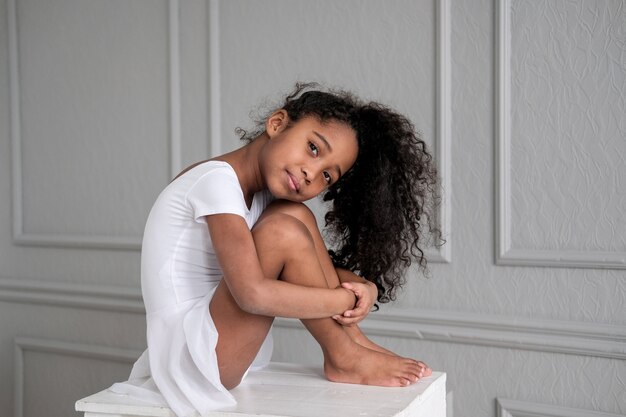 La ballerina afroamericana in un costume da ginnastica bianco si siede su una sedia di legno