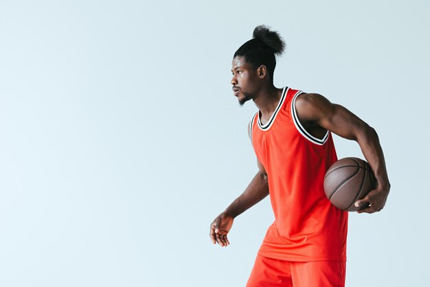 African american basketball player holding ball and looking away isolated on grey