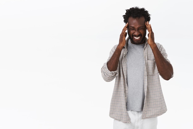 African-american bearded guy suffering unbearable headache, touching temples, squinting and making grimace