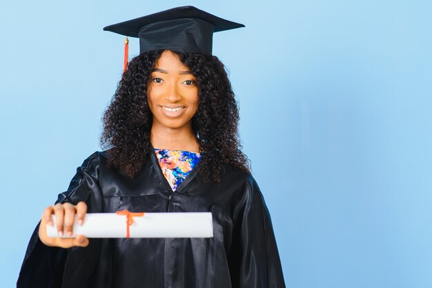 African-American beautiful woman in a black robe and hat, on a blue isolated background smiles.